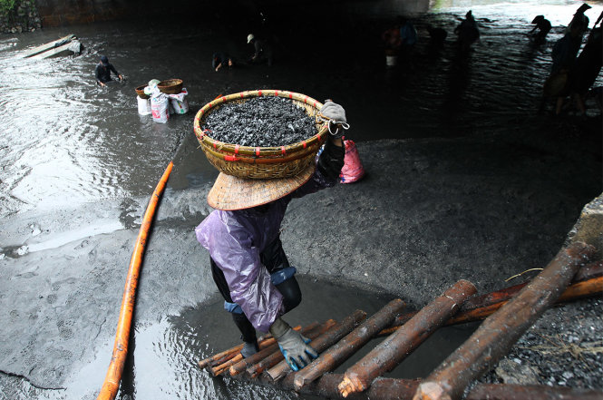 Mỗi thúng than có trọng lượng gần 20kg, việc di chuyển lên bờ qua một chiếc thang gỗ giữa trời mưa tiềm ẩn nhiều nguy cơ rủi ro - Ảnh: Nguyễn Khánh